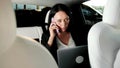Busy businesswoman talking on the mobile phone and typing on the laptop during trip in the car. Transport, technology Royalty Free Stock Photo