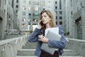 Busy caucasian woman having phone business discussion while holding coffee cup, papers and laptop near office building. Office Royalty Free Stock Photo