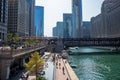 Busy Chicago scene at Chicago River with el train crossing water, children playing at splash pad, Wacker Dr. commuters,