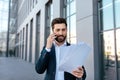Busy confident attractive young caucasian man with beard calls by smartphone, works with documents