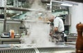 Busy day. Back view of male chef in apron cutting a meat while standing in a restaurant kitchen Royalty Free Stock Photo