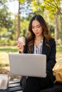 A busy, elegant Asian businesswoman is working remotely on her laptop in a park while having lunch Royalty Free Stock Photo