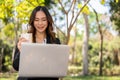 A busy, elegant Asian businesswoman is working remotely on her laptop in a park while having lunch Royalty Free Stock Photo