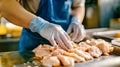 In a busy factory, a diligent worker in a blue apron and gloves skillfully prepares fresh chicken fillets for processing on a Royalty Free Stock Photo
