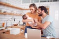 Busy Family In Kitchen At Breakfast With Mother Caring For Baby Son