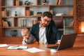 Busy father. Businessman in formal clothes is working indoors. With toddler Royalty Free Stock Photo