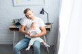 busy father sitting on chair with notebook, talking on smartphone and holding baby daughter