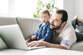 Busy father working on laptop with baby in front