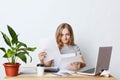 Busy female enterpreneur looking through documents, sitting at table in her cabinet, working with laptop computer, smart phone and Royalty Free Stock Photo