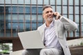 Busy happy mature business man making phone call using laptop sitting outside. Royalty Free Stock Photo