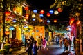 Busy Hoian street in the historic center with colorful Vietnamese lantern lamps, tourists and shops on the side at night. Hoi An