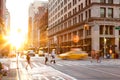 Busy intersection of 23rd Street and 5th Avenue in Manhattan is crowded with people and traffic as the sun sets in the background.