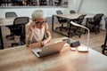 Busy lady. Young and beautiful tattooed business woman adjusting her eyewear and working with laptop while sitting in Royalty Free Stock Photo