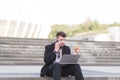 A busy man in a business suit sits on laptops with a laptop on his lap, eats a sandwich and speaks on a mobile phone Royalty Free Stock Photo