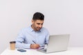 Busy man employee working on laptop and writing paper notebook, preparing report doing paperwork Royalty Free Stock Photo