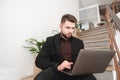 Busy man sits on the floor against stairs and plants and works on a computer.Copyspace