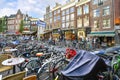 A busy market street in Amsterdam crowded with a mass of parked bicycles as locals and tourists enjoy the sidewalk cafes and shops