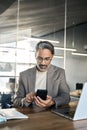 Busy mature business man sitting at office desk using mobile phone. Vertical. Royalty Free Stock Photo