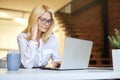 Busy mature businesswoman in glasses using laptop while doing some paperwork at the office