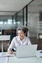 Middle aged businesswoman working in office using laptop writing notes. Vertical Royalty Free Stock Photo