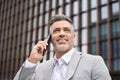 Busy mid aged business man making call talking on phone standing on city street. Royalty Free Stock Photo