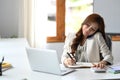 Busy millennial working woman negotiating with client via mobile phone and making notes on notebook