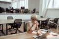 Busy morning. Young beautiful tattooed business woman in eyewear drinking coffee and working with laptop while sitting Royalty Free Stock Photo