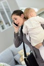 Busy mother holding her baby and talking on the phone Royalty Free Stock Photo