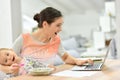 Busy mother working on laptop and feeding her baby