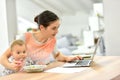 Busy mother working on laptop and feeding her baby