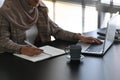 A busy muslim woman in headscarf is working on her project with computer laptop and taking notes. Royalty Free Stock Photo