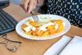 Busy office woman eats lunch at her workplace without interrupting work, a plate with healthy food on the desk, top view Royalty Free Stock Photo