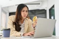 Busy and overworked Asian businesswoman eating a sandwich while using laptop