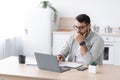 Busy pensive middle aged european businessman in glasses working at computer on minimalist kitchen interior