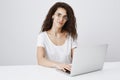 Busy photographer editing photos. Portrait of attractive fashionable female student with curly hair sitting near laptop Royalty Free Stock Photo