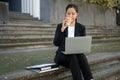 A busy Asian businesswoman is sipping coffee and reading an urgent email on her laptop in the city