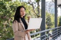 A busy Asian businesswoman is sipping coffee and working on her laptop outdoors on the skywalk Royalty Free Stock Photo