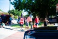 Busy residential road intersection with blurred diverse group of people watching July Fourth parade, lawn flags display front of Royalty Free Stock Photo