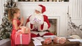 Busy Santa sorting chidlren`s letters while cute little helper bringing him a gift