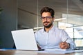 Busy smiling young Latin business man working in office using laptop writing. Royalty Free Stock Photo