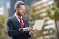 busy successful businessman in suit working on laptop standing outdoor, modern life