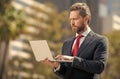 busy successful businessman in suit working on laptop standing outdoor, modern life