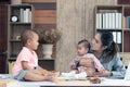 Busy woman trying to work while babysitting two kids.  Young Asian mother talking and playing with two children playing around her Royalty Free Stock Photo