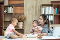 Busy woman trying to work while babysitting two kids.  Young Asian mother talking and playing with two children playing around her Royalty Free Stock Photo