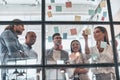 Busy with work. Group of young modern people in smart casual wear using adhesive notes while standing behind the glass wall in th