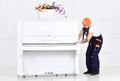 Busy worker in orange protective helmet and blue overall moving grand piano isolated on white background. White piano