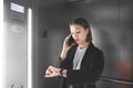 Busy young businesswoman is looking at her watch and talking the phone in the elevator. Tied up female employee is checking time Royalty Free Stock Photo