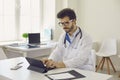 Serious young male doctor sitting at desk in office and working on tablet computer Royalty Free Stock Photo