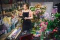 Busy young florist stand at table and hold black planchette and writedown. She is surround with different plants and Royalty Free Stock Photo