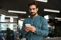 Busy young Latin business man using cellphone at work standing in office. Royalty Free Stock Photo